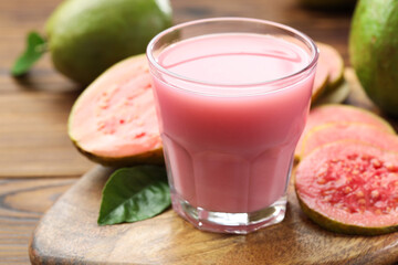 Tasty guava juice in glass, leaves and fruits on wooden table, closeup