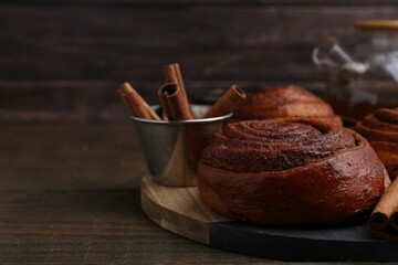 Delicious cinnamon roll buns and spices on wooden table, closeup