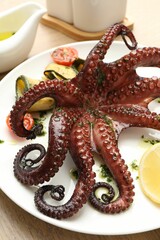 Obraz premium Fried octopus with herb sauce, lemon and vegetables on wooden table, closeup