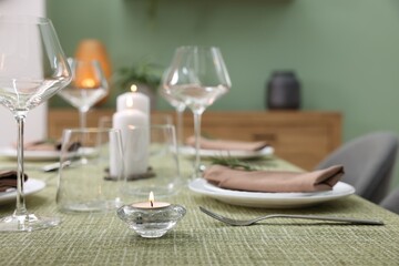 Stylish table setting with olive tablecloth, glasses and candles indoors, closeup