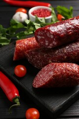 Different smoked sausages, tomatoes and chili pepper on black wooden table, closeup