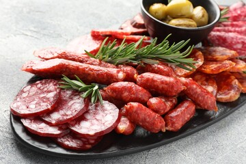 Different smoked sausages, olives and rosemary on grey table, closeup