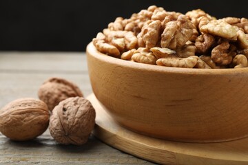 Peeled walnuts in bowl and whole ones on wooden table, closeup