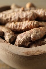 Raw turmeric roots in wooden bowl, closeup