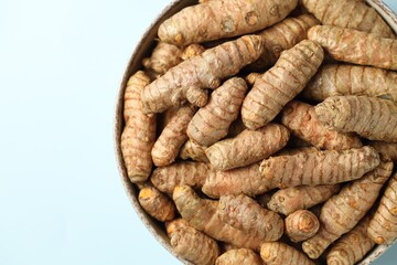 Tumeric rhizomes in bowl on light blue background, top view
