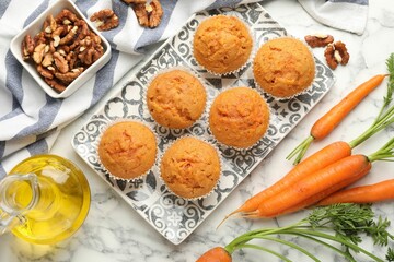 Tasty carrot muffins, fresh vegetables and walnuts on white marble table, flat lay