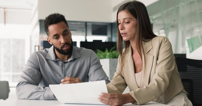 Serious young business legal advisor giving consultation, advice, lawyer support to African American businessman, customer, client, explaining financial report, contract, agreement text
