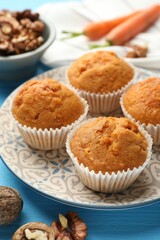 Tasty carrot muffins and walnuts on light blue wooden table, closeup