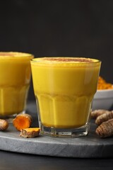 Delicious turmeric latte, powder and rhizomes on black wooden table, closeup