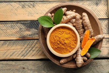 Aromatic turmeric powder in bowl, fresh roots and leaves on wooden table, top view. Space for text