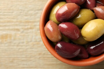 Tasty olives in bowl on wooden table, top view. Space for text