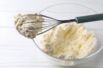 Bowl with whisk and whipped cream on white wooden table, closeup