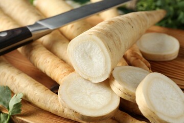 Whole and cut parsley roots with knife on wooden table, closeup