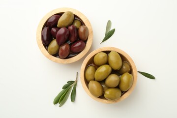 Tasty marinated olives in bowls and leaves on white table, flat lay