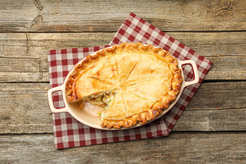 Tasty homemade pie with chicken and vegetables in baking dish on wooden table, top view