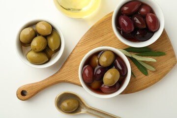 Tasty marinated olives, leaves and oil on white table, flat lay