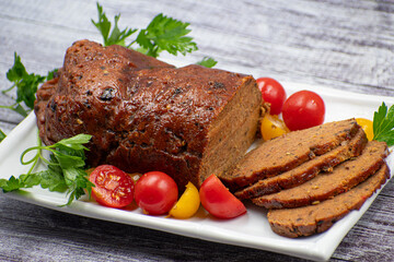 Vegan meat alternative- seitan seasoned with spiced, glazed with BBQ sauce. White plate, sliced, wooden table.