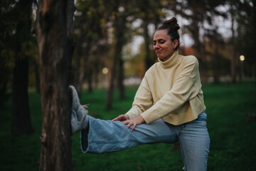 A young girl performs leg stretches outdoors in a green park, dressed in casual autumn clothes....
