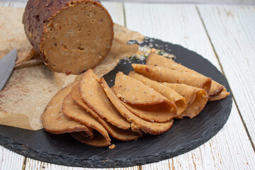 Seitan shaped and cooked in ham press, sliced on slate board. Vegan protein, plant based alternative to meat.