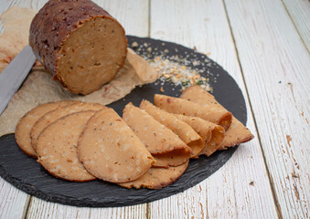 Seitan shaped and cooked in ham press, sliced on slate board. Vegan protein, plant based alternative to meat.
