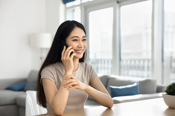 Beautiful Asian woman sitting at table in cozy living room, smile, lead pleasant conversation on...