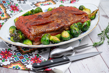 Vegan pork bellly roast made with seitan and starch, served on oval plate along with roasted Brussels sprouts. Wooden table, stylish setting