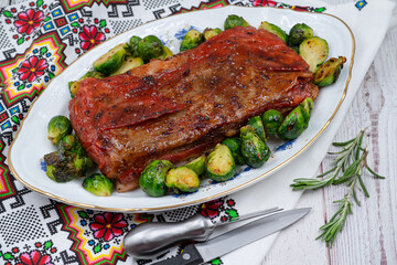 Vegan pork bellly roast made with seitan and starch, served on oval plate along with roasted Brussels sprouts. Wooden table, stylish setting