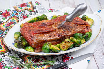 Vegan pork bellly roast made with seitan and starch, served on oval plate along with roasted Brussels sprouts. Wooden table, stylish setting