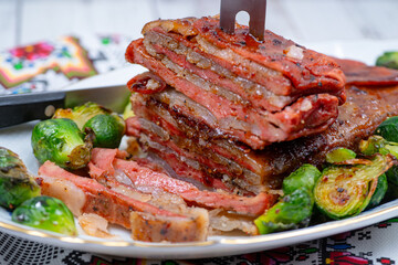 Vegan pork bellly roast made with seitan and starch, served on oval plate along with roasted Brussels sprouts. Wooden table, stylish setting