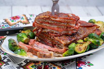 Vegan pork bellly roast made with seitan and starch, served on oval plate along with roasted Brussels sprouts. Wooden table, stylish setting