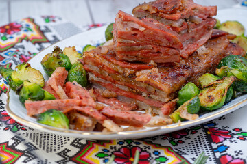 Vegan pork bellly roast made with seitan and starch, served on oval plate along with roasted Brussels sprouts. Wooden table, stylish setting