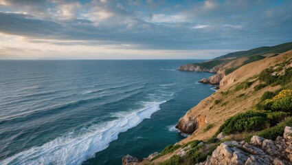 Fototapeta premium Coastal landscape view with rolling waves and cliffs under a cloudy sky during sunset with Copy Space for text placement