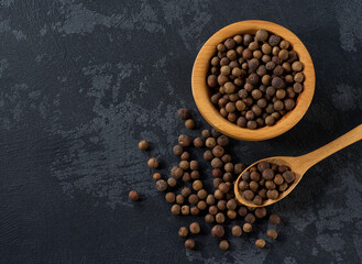 allspice or Jamaican pepper seeds in a wooden bowl on a black stone table, top view.