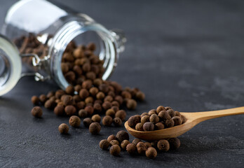 allspice or Jamaican pepper in a wooden scoop and in glass storage jar on a black kitchen table,...