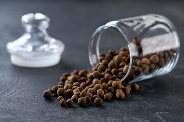 allspice or Jamaican pepper spill out of a glass storage jar on a black kitchen table, selective focus.
