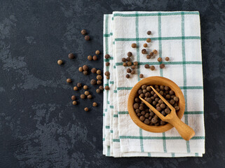 Wooden bowl with allspice or Jamaican pepper on a black kitchen table, top view.