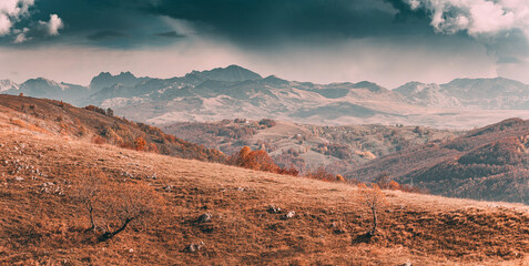 Fototapeta premium Scenic landscape showcasing the beauty of nature with rolling hills, colorful autumn foliage, and majestic mountains under a dramatic cloudy sky