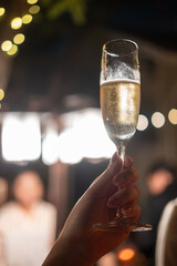 A hand holding a glass of Prosecco or sparkling wine, with bokeh lighting in the background