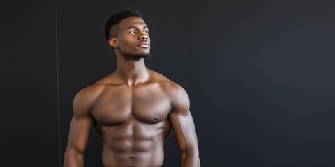 A man with a muscular chest stands in front of a black wall. He looks focused and determined