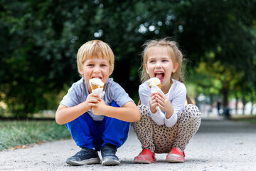 Portrait two cute cheerful children enjoy ice cream together at nature city park path on hot summer...