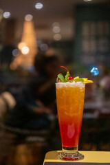Close up view of orange cocktail, with cherry and sliced orange on top. On the table with bokeh background