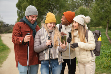 Group of young hikers using smartphone and smiling during trekking day in the nature