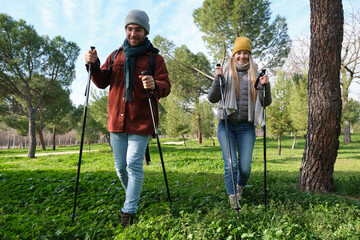 Young couple practicing nordic walking in a green park during a sunny winter day