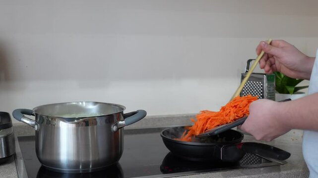 Adding grated carrots to a frying pan beside a pot