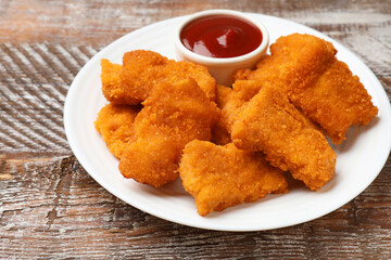 Delicious chicken nuggets with ketchup on wooden table, closeup
