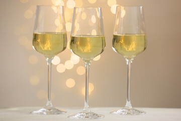 Tasty white wine in glasses on table against grey background with blurred lights, bokeh effect
