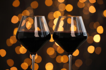 Tasty red wine in glasses against dark background with blurred lights, closeup. Bokeh effect