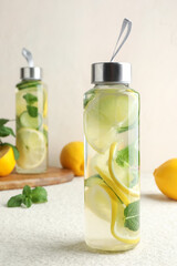 Lemon water with mint in bottles and fresh fruits on beige table