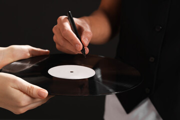 Singer signing autograph on vinyl record against black background, closeup