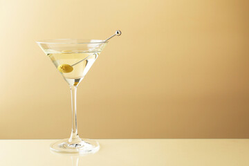 Martini cocktail with olive in glass on beige table, space for text